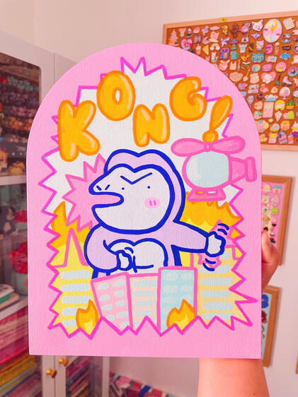 Acrylic painting of King Kong batting away a helicopter in the city, framed by a jagged pink border.